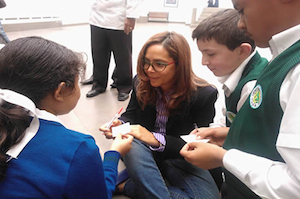 La ministra de educación Gina Parody sentada en el piso rodeada de una niña y dos niños con uniformes del colegio